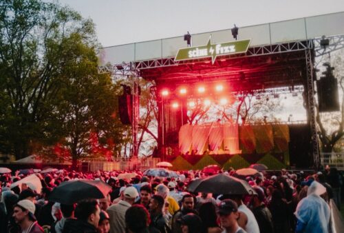 A crowd of people stands before a lit stage outdoors